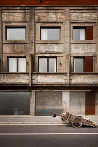 A weathered concrete facade of a multi-story building with windows and doors.
