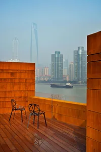 A wooden terrace overlooking modern urban buildings with metal accents and a ship on the water.