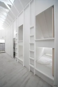 A minimalist bedroom featuring concrete walls and floors, with built-in bunk beds and shelves.
