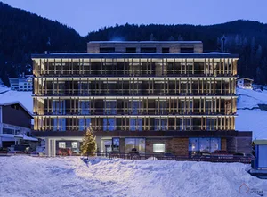 Modern hotel building with glass balconies and concrete structure, illuminated at dusk in a snowy landscape