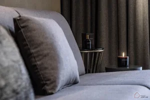 A modern living room featuring a gray sofa adorned with botanical candles and a side table with a small bottle of lotion.