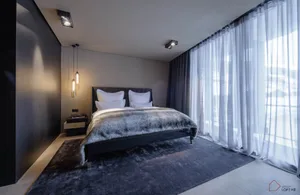 Modern minimalist bedroom with a bed featuring textured fabric and glass elements, situated in a spacious room with a large w