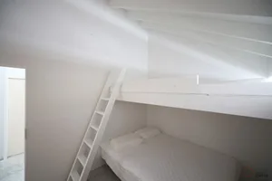 A minimalist bedroom with a white bunk bed and a white ladder.
