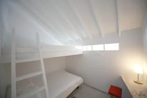 A minimalist bedroom with white walls, a bunk bed, a desk, and a lamp.