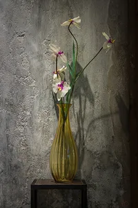 An industrial-style vase filled with flowers on a black table against a textured wall background.
