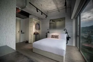 Modern industrial-style bedroom with concrete walls, large window, and minimalist furniture.