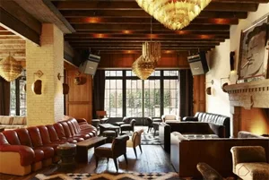 A cozy, industrial-themed hotel lounge featuring brick walls, wooden accents, leather furniture, and metallic chandeliers.