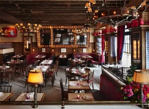 An industrial-themed restaurant interior featuring wooden tables, leather benches, and fabric upholstered chairs.