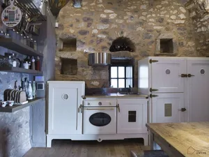 A rustic industrial-style kitchen with white cabinetry, metallic accents, and stone walls.