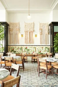 A restaurant seating area featuring macrame wall hangings and tropical-themed cushions on the bench
