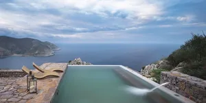A modern swimming pool with a metal and glass design overlooking a scenic coastal view.