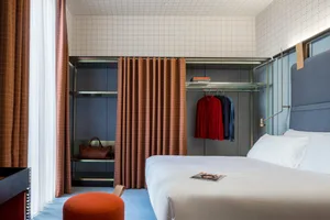 Modern minimalist bedroom with blue carpet, orange pouf, and organized closet