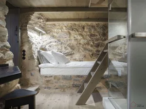 A minimalist bedroom with stone walls, a bed, and a glass stair railing.