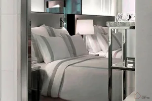 A minimalist bedroom with white-on-white striped bedding and a sleek, modern headboard and bedside table.