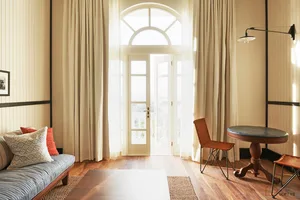 A modern minimalist living room featuring a grey couch with orange and white pillows, a wooden coffee table, and hardwood flo