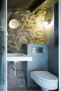 Modern bathroom with concrete and stone walls, featuring a white sink and toilet.