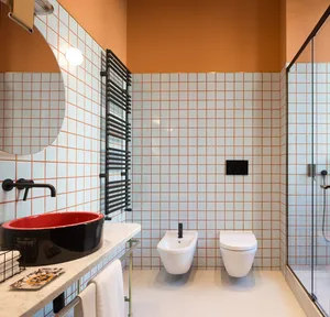 Modern bathroom featuring white and orange tiled walls, a red sink, and a minimalist design