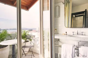 White tiled bathroom with a glass door and a balcony with a table and chairs.