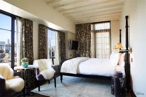 Modern bedroom featuring a bed with white linens, a fur-covered accent chair, and floral arrangement on a small round table w