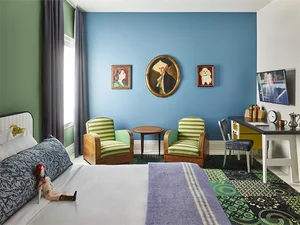 A modern bedroom with green and blue walls, a bed, chairs, and a coffee table.
