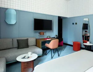 A modern hotel suite featuring a comfortable sofa, a flat-screen TV, a desk with a chair, and a coffee table with a magazine 