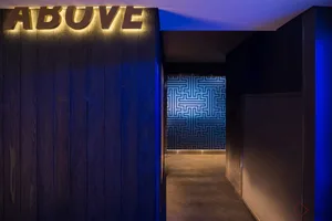 A modern interior corridor with a wooden light brown paneled wall and dark blue geometric tile floor.