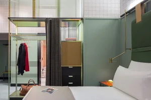 A modern minimalist bedroom with a green headboard, white bedding, and a glass wardrobe with a black curtain.