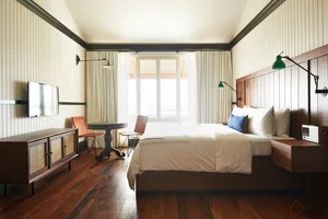 A minimalist bedroom with a wooden floor, white curtains, and a large window.