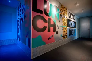 A vibrant, minimalist corridor featuring colorful graffiti-style mural art with phrases such as 'I HAVE YOUR BREAKFAST', 'GOO
