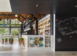A modern restaurant bar with wooden tables, metal stools, and a glass-fronted bar.