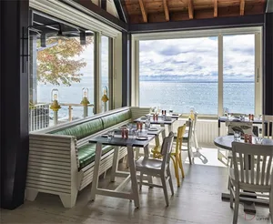 A modern restaurant with a sea view, featuring wooden furniture and large windows.