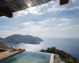 A scenic view of a vacation home featuring an infinity pool overlooking the ocean and distant mountains.