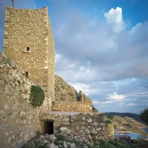 Ancient ruins of a stone structure with a tall tower amidst a cloudy sky.