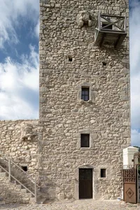 A tall, ancient stone tower with a wooden door and a wooden balcony.