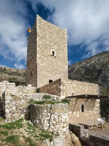 A medieval stone tower with a flag on top, set against a mountainous backdrop.