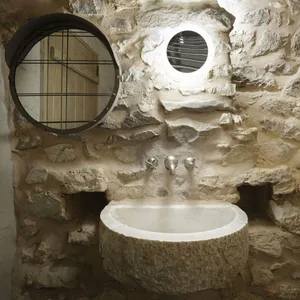 A minimalist bathroom with a stone wall, sink, and round mirror.