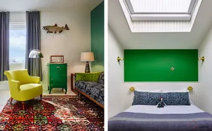 A modern bedroom with a bright yellow armchair, a green dresser, a bed with a green headboard and blue bedding, and a colorfu
