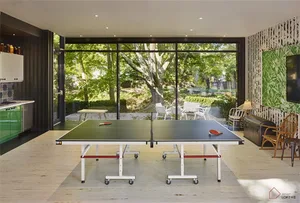 A modern game room featuring a wooden ping pong table, white chairs, and a green wall with a leaf pattern.