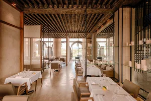 Modern restaurant interior with industrial-style decor featuring wooden ceiling, glass shelves, and concrete flooring.