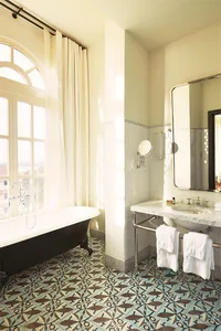 A modern bathroom featuring a clawfoot bathtub, white marble sink, and pastel patterned ceramic flooring.