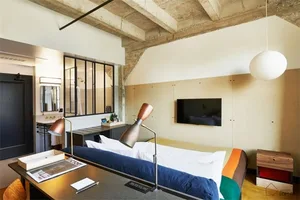 Industrial-style bedroom with exposed brick walls, concrete ceiling beams, and a bed with white linens.