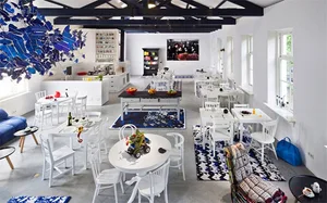 Industrial-style cafe interior with concrete and metal elements, featuring white tables and chairs.