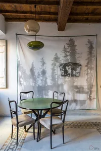 A dining area featuring a green table, chairs, and a fabric screen with a forest painting in the background.