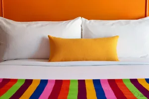 A minimalist bedroom featuring a white bed with a yellow blanket and a bright pillow.