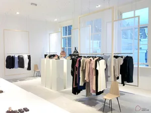 A minimalist clothing retail store with white canvases and wooden chairs.