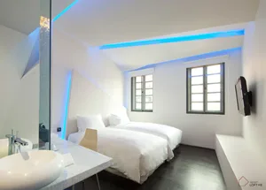 A minimalist bedroom with white bedding, a sink, and a mirror.