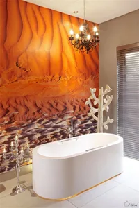 A contemporary bathroom featuring an acrylic bathtub and a chandelier, with a wall mural depicting a desert landscape.