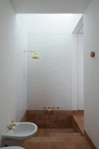 Modern bathroom with brick walls and a white sink under a golden shower faucet.