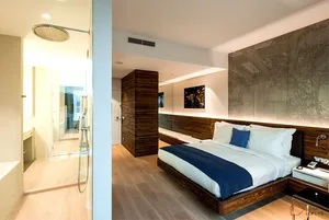 Bedroom featuring a modern wooden bed, white sheets, and a blue throw blanket, with minimalist decor and glass shower enclosu