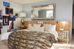 A modern bedroom with a bed covered in a plush fur blanket, framed photographs on the wall, and a wooden headboard.